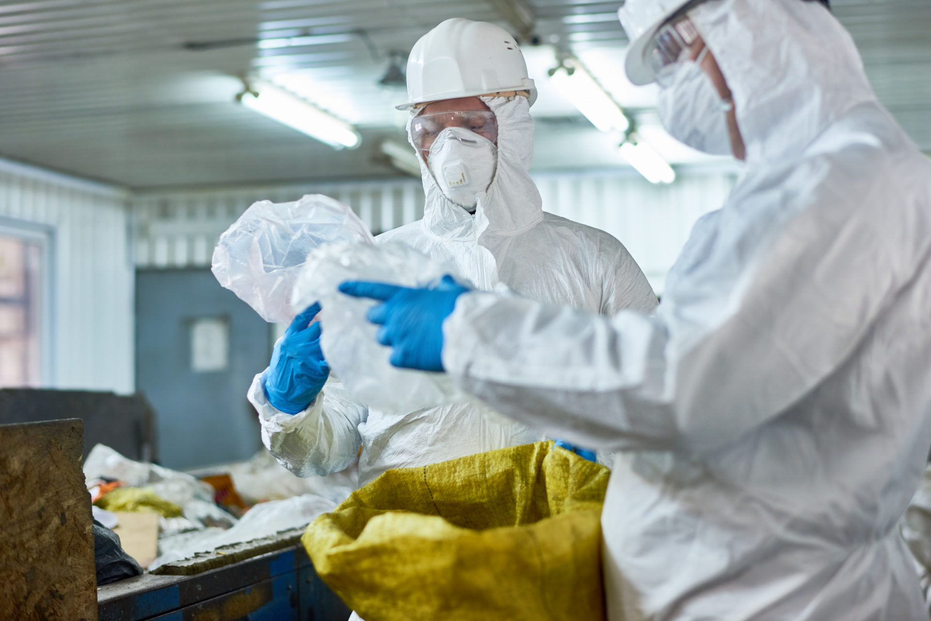 Portrait of two workers  wearing biohazard suits working at waste processing plant sorting trash and reusable plastic standing by conveyor belt