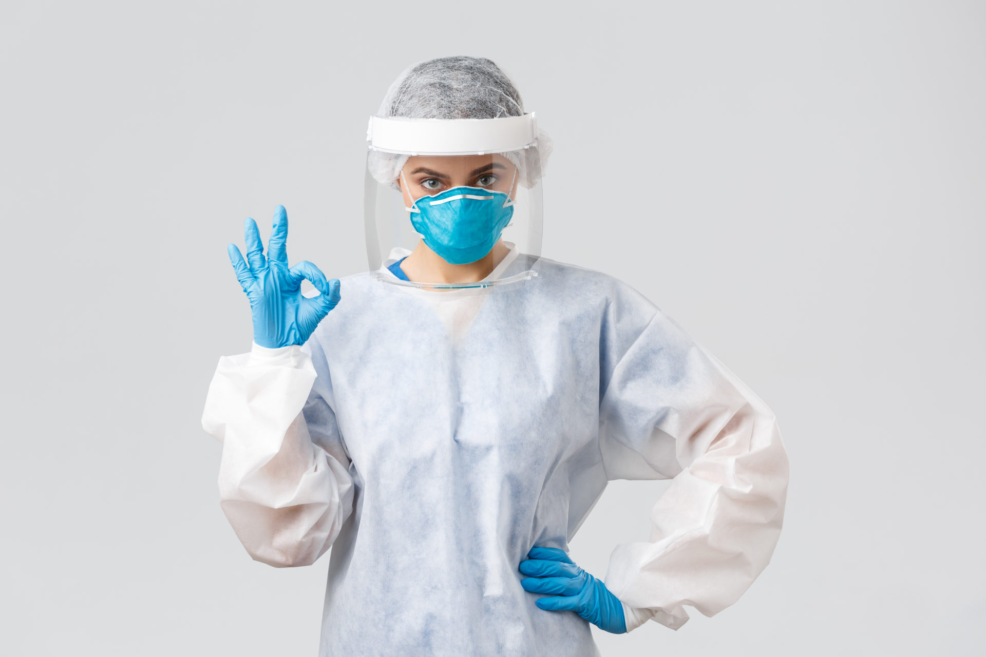 Covid-19, preventing virus, health, healthcare workers and quarantine concept. Serious doctor, professional nurse in PPE, protective suit, respirator and gloves, make okay sign, guarantee.